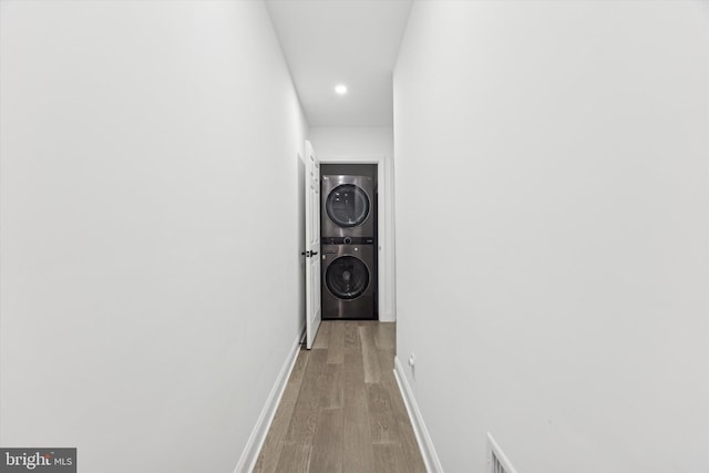 hallway with light wood-style flooring, recessed lighting, stacked washer and clothes dryer, and baseboards