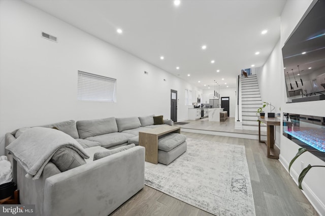 living room with stairs, light wood-type flooring, visible vents, and recessed lighting