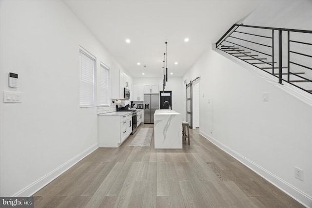 kitchen featuring a barn door, stainless steel appliances, a sink, white cabinetry, and a center island with sink