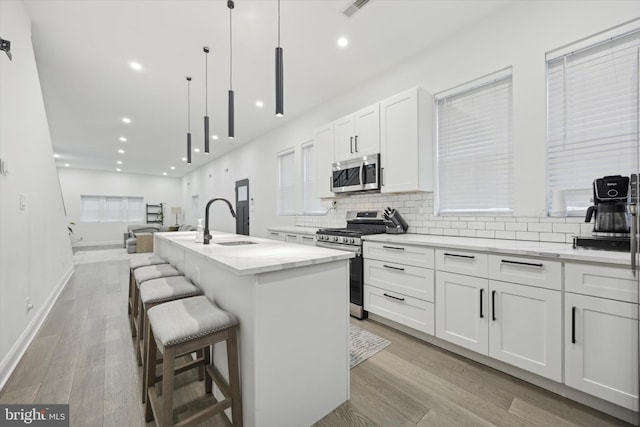 kitchen featuring decorative light fixtures, appliances with stainless steel finishes, a center island with sink, and white cabinetry