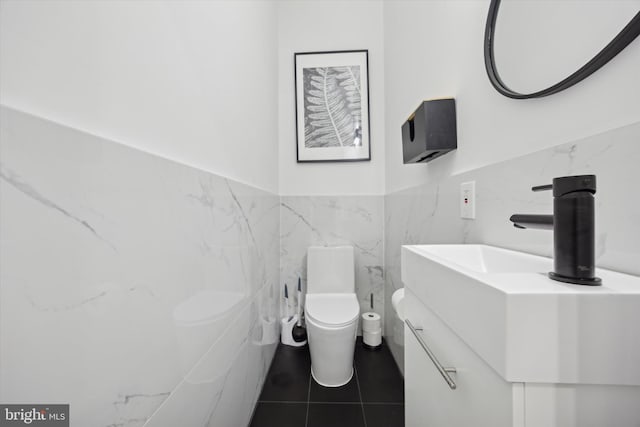 half bath with tile patterned flooring, toilet, a wainscoted wall, vanity, and tile walls