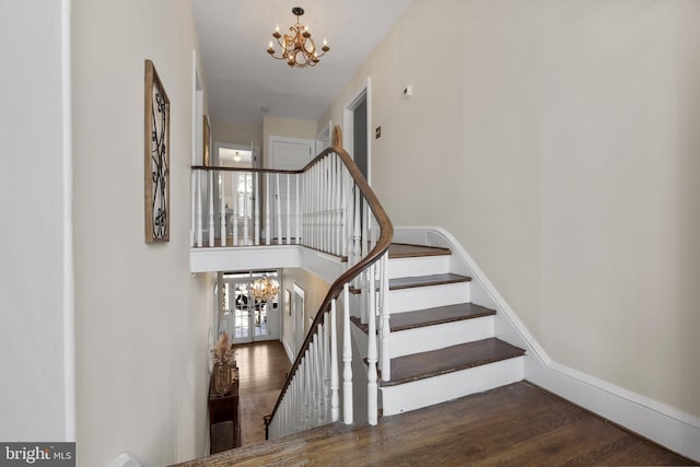 stairway featuring baseboards, wood finished floors, a towering ceiling, and an inviting chandelier