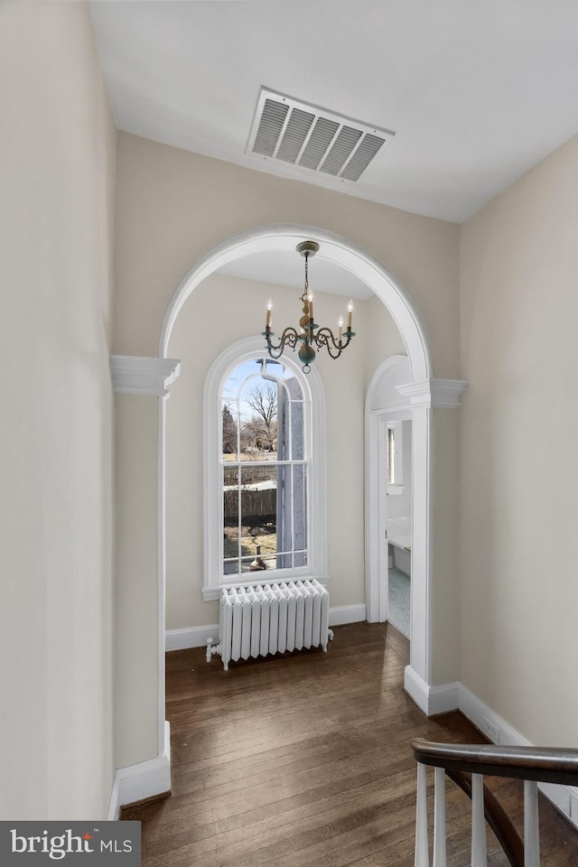 corridor featuring a notable chandelier, radiator, visible vents, wood finished floors, and baseboards