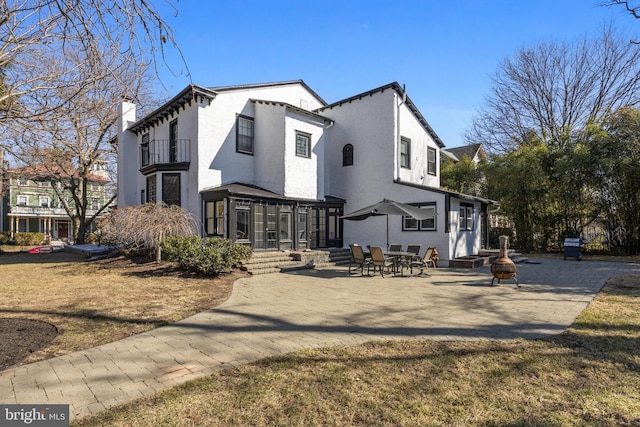 exterior space with a patio, a balcony, a sunroom, stucco siding, and a chimney