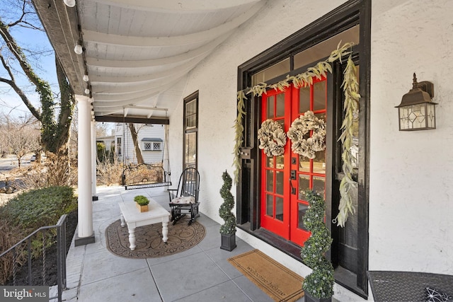 doorway to property featuring covered porch, french doors, and stucco siding