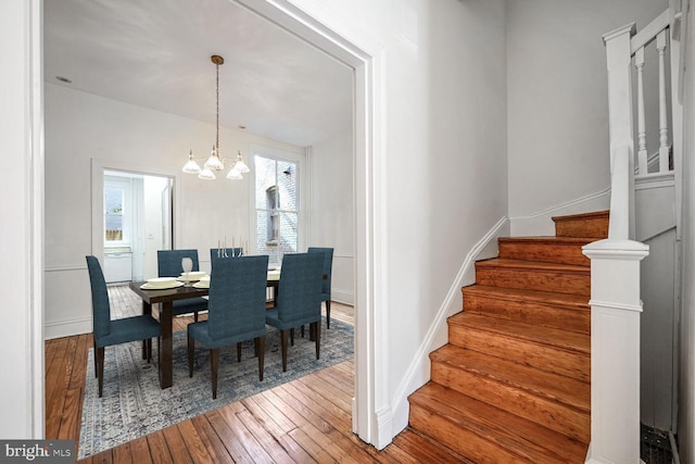 dining space with baseboards, stairway, wood finished floors, and an inviting chandelier