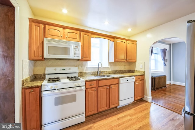 kitchen featuring sink, white appliances, light hardwood / wood-style flooring, backsplash, and light stone counters