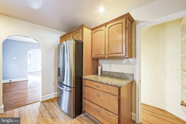 kitchen with stainless steel refrigerator with ice dispenser, decorative backsplash, light stone counters, and light wood-type flooring