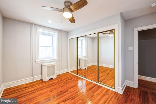 unfurnished bedroom with ceiling fan, wood-type flooring, a closet, and radiator heating unit