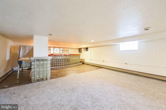 basement featuring baseboard heating, carpet flooring, and a textured ceiling