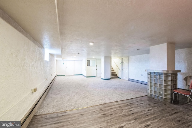 basement featuring baseboard heating, hardwood / wood-style floors, and a textured ceiling