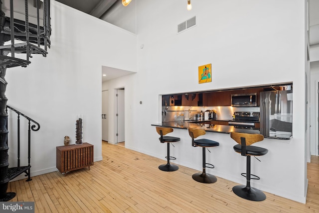 kitchen with stainless steel appliances, a high ceiling, and light wood-type flooring