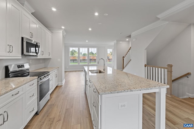 kitchen featuring sink, stainless steel appliances, light stone countertops, white cabinets, and a center island with sink