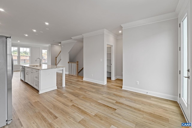 kitchen featuring white cabinetry, sink, stainless steel appliances, light stone countertops, and a center island with sink