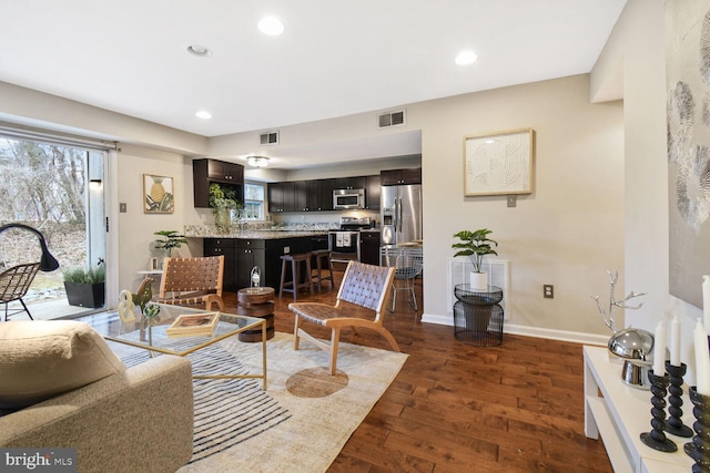 living room featuring baseboards, dark wood-style flooring, visible vents, and a healthy amount of sunlight