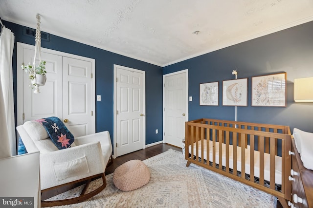 bedroom with multiple closets, ornamental molding, a nursery area, and dark hardwood / wood-style floors