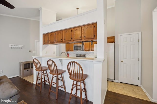 kitchen with appliances with stainless steel finishes, backsplash, a kitchen breakfast bar, and kitchen peninsula