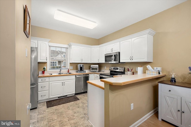 kitchen with white cabinetry, appliances with stainless steel finishes, kitchen peninsula, and sink