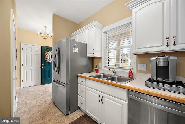 kitchen with appliances with stainless steel finishes, sink, white cabinets, and a chandelier