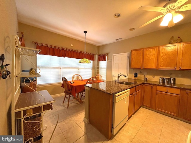 kitchen featuring light tile patterned floors, dark stone countertops, white dishwasher, and a sink