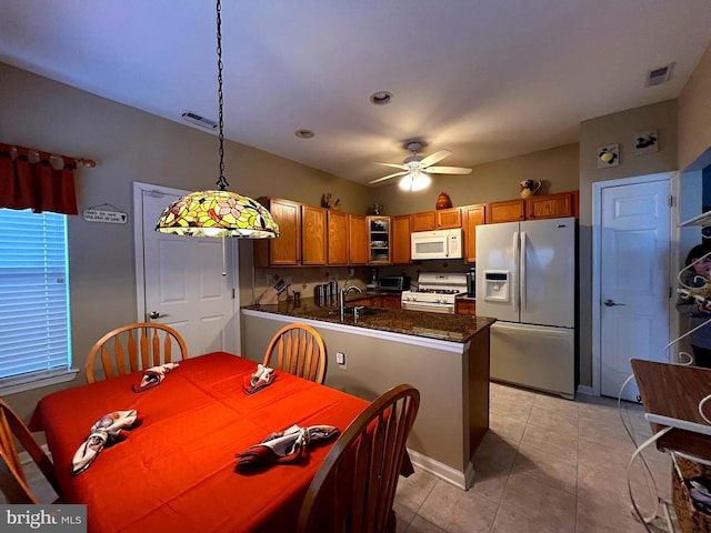 kitchen featuring a peninsula, white appliances, a sink, visible vents, and brown cabinets