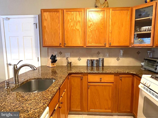 kitchen featuring dark stone counters, tasteful backsplash, a sink, and white range with gas cooktop