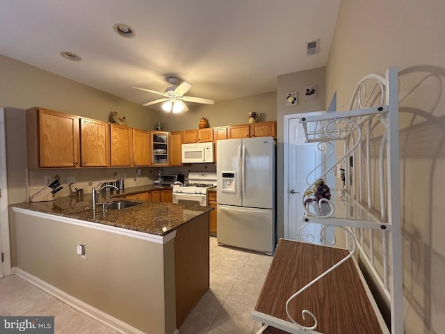 kitchen featuring visible vents, a sink, dark stone countertops, white appliances, and a peninsula