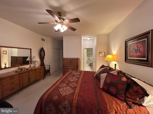 bedroom with a ceiling fan, light colored carpet, visible vents, and ensuite bath