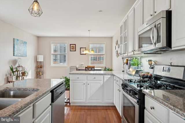 kitchen featuring stone countertops, decorative light fixtures, light wood-type flooring, stainless steel appliances, and white cabinets