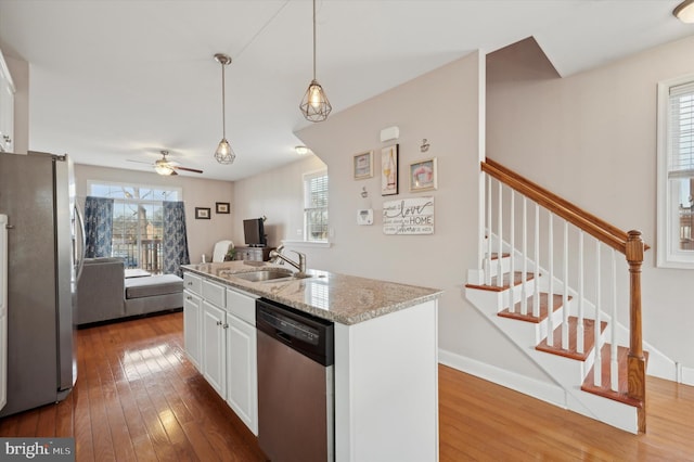 kitchen featuring sink, white cabinets, stainless steel appliances, light stone countertops, and a center island with sink