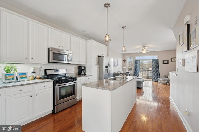 kitchen featuring an island with sink, appliances with stainless steel finishes, white cabinets, and light stone counters