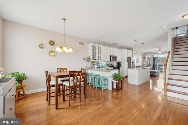 dining space with ceiling fan with notable chandelier and light hardwood / wood-style floors