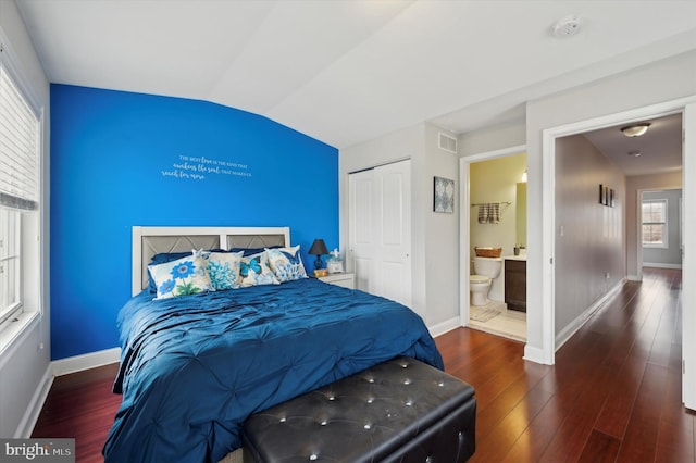 bedroom featuring dark hardwood / wood-style flooring, ensuite bath, lofted ceiling, and a closet