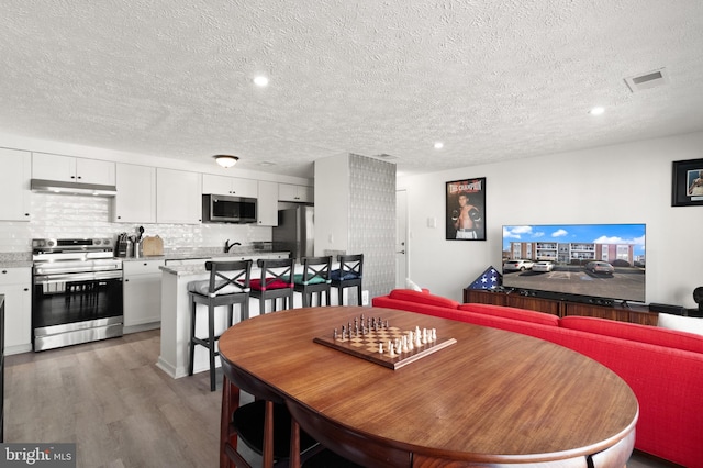 dining area featuring visible vents, light wood-style flooring, and a textured ceiling