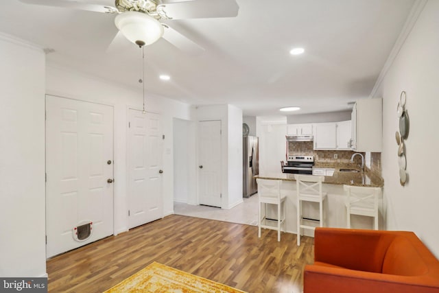 kitchen with appliances with stainless steel finishes, white cabinetry, a kitchen bar, kitchen peninsula, and light hardwood / wood-style flooring