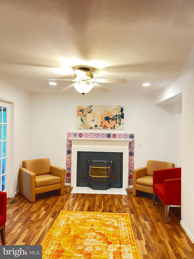 living room with hardwood / wood-style flooring, ornamental molding, a wood stove, and ceiling fan