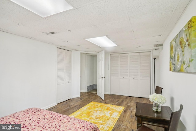 bedroom with dark hardwood / wood-style flooring, a paneled ceiling, and multiple closets