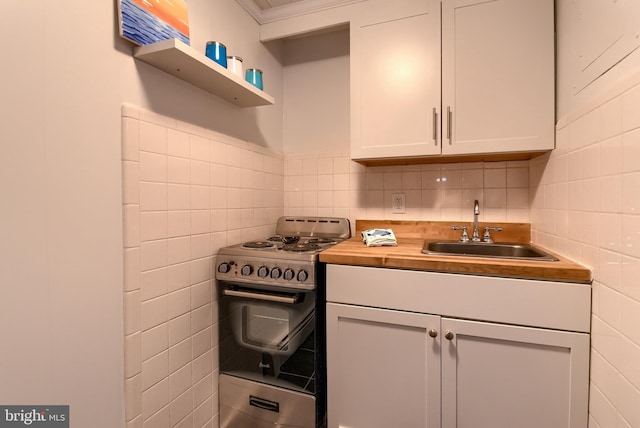 kitchen with butcher block counters, stainless steel range oven, sink, tile walls, and white cabinets