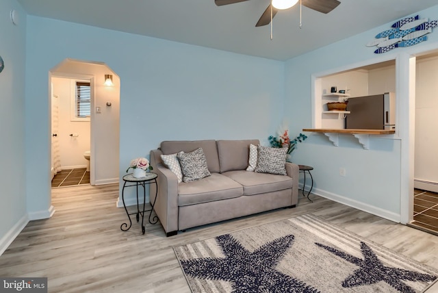 living room with ceiling fan, a baseboard heating unit, and light wood-type flooring