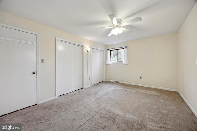 unfurnished bedroom featuring multiple closets, ceiling fan, and light carpet