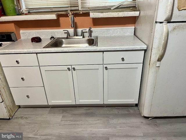 kitchen featuring white cabinetry, sink, light hardwood / wood-style flooring, and white fridge