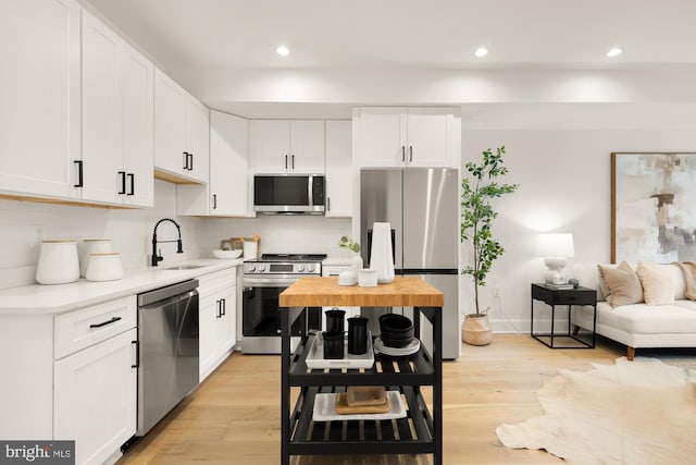 kitchen with appliances with stainless steel finishes, tasteful backsplash, white cabinetry, sink, and light hardwood / wood-style floors