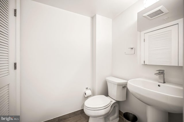 half bath featuring toilet, visible vents, a sink, and wood finished floors