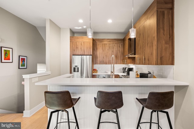 kitchen featuring a peninsula, brown cabinetry, light countertops, and stainless steel fridge with ice dispenser