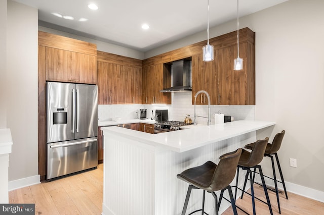 kitchen featuring appliances with stainless steel finishes, decorative backsplash, a peninsula, and wall chimney exhaust hood