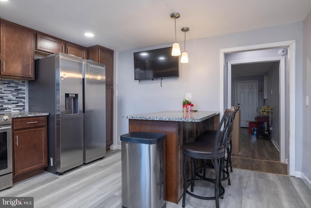 kitchen featuring appliances with stainless steel finishes, pendant lighting, light stone countertops, a breakfast bar area, and decorative backsplash