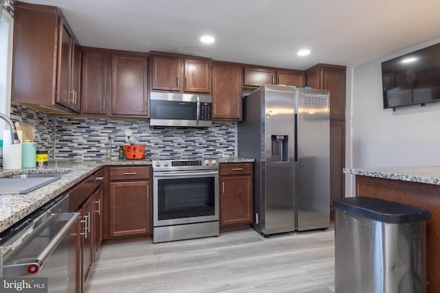 kitchen with stainless steel appliances, light stone counters, light hardwood / wood-style floors, backsplash, and sink