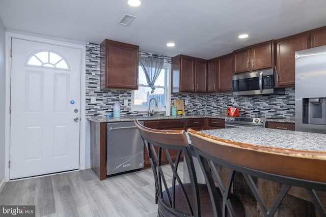 kitchen with appliances with stainless steel finishes, sink, light hardwood / wood-style flooring, light stone countertops, and tasteful backsplash