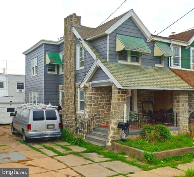 view of front of home with stone siding, a porch, and a chimney