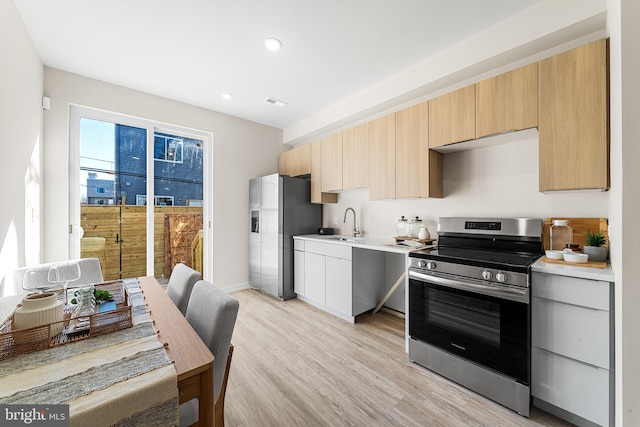 kitchen with recessed lighting, stainless steel appliances, a sink, light countertops, and light wood-type flooring